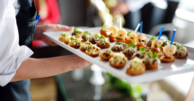 A server holding a long plate of appetizers