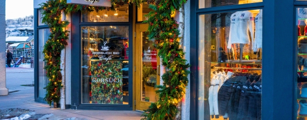 A storefront of Gorsuch Ski Cafe decorated with festive garlands and lights, showcasing winter apparel through large windows.