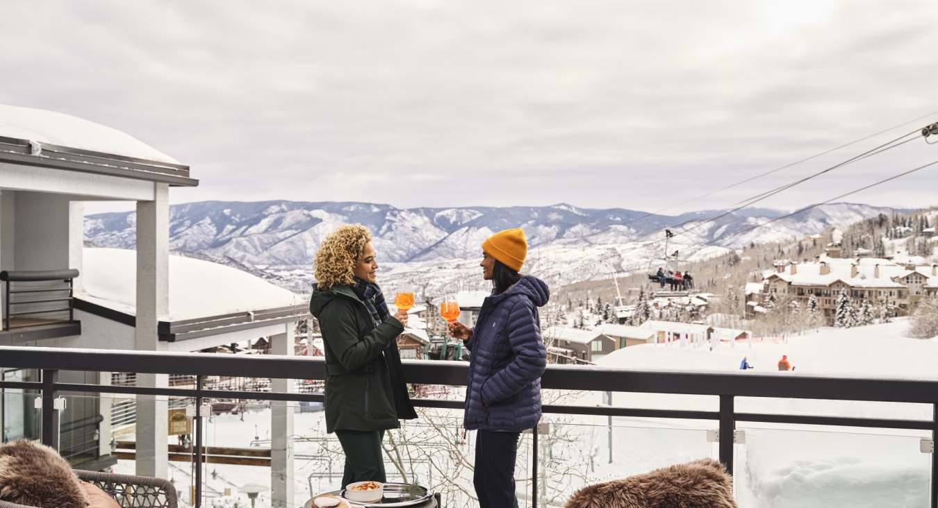 two women on snowy balcony overlooking mountains
